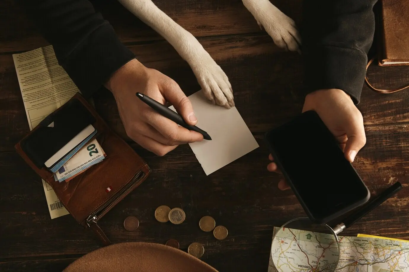 Крупный план: руки мужчины держат смартфон и записывают план маршрута приключения на листе бумаги на старом деревянном столе.
